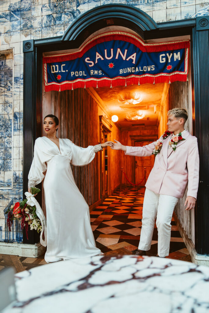Two brides stand side by side, holding hands in a vibrant entryway.
