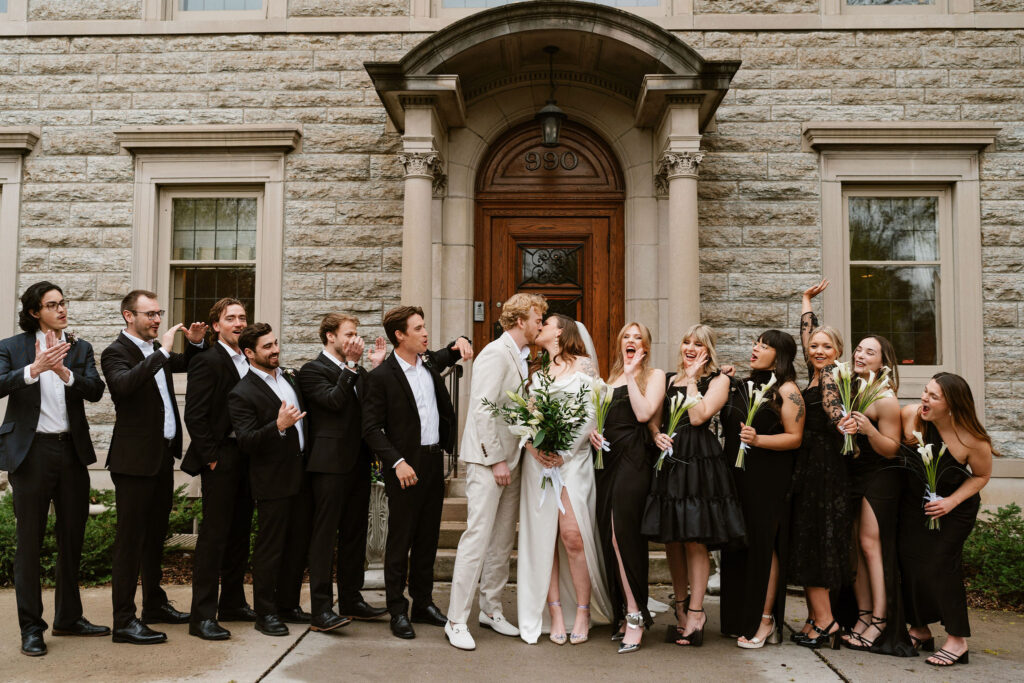 Bride and groom kiss surrounded by their wedding party