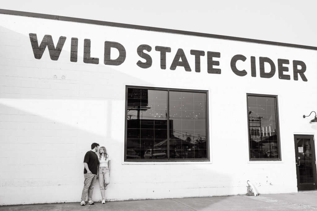 A couple leans against the building of Wild State Cider in Minnesota