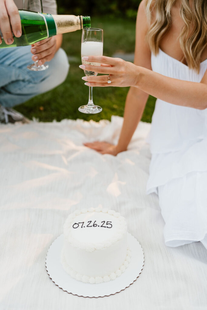 A couple does a champagne toast with their wedding date cake below them