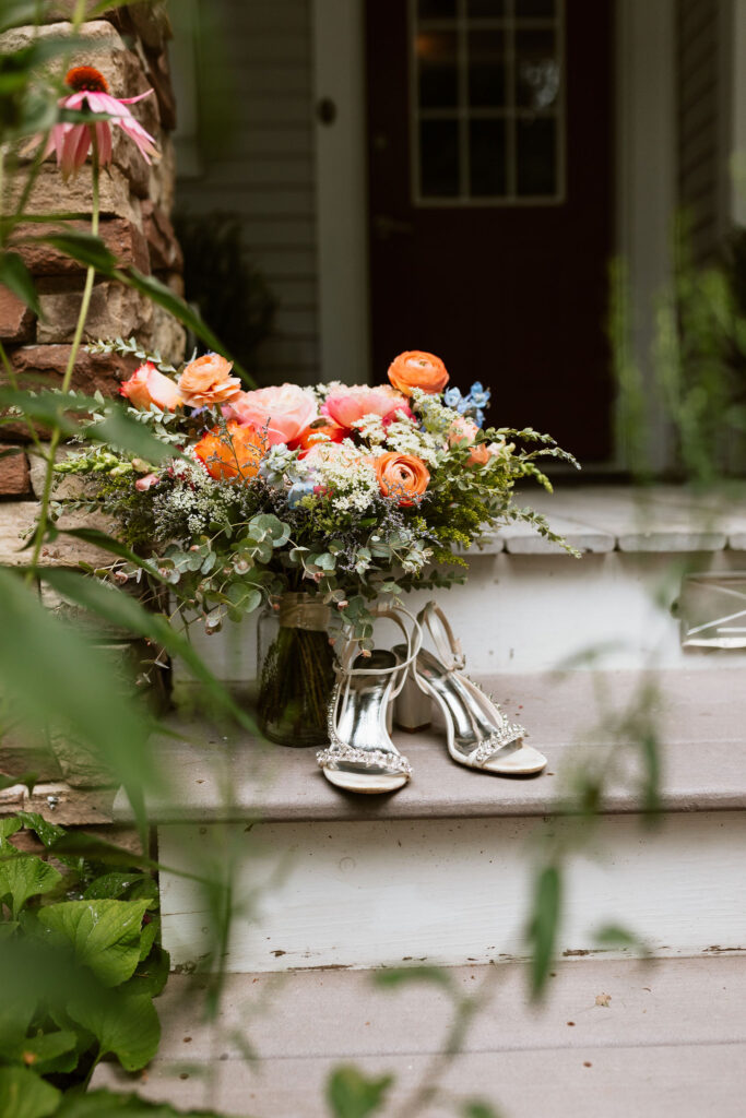 A colorful wedding bouquet sits on the porch steps by the brides heels