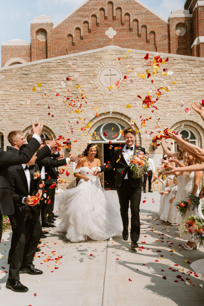 Wedding guests toss up colorful flower petals as the bride and groom walk out of the church after their Wisconsin wedding ceremony