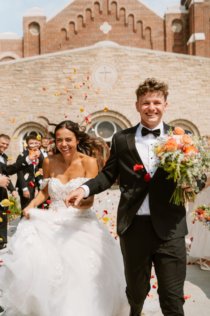 Wedding guests toss up colorful flower petals as the bride and groom walk out of the church after their Wisconsin wedding ceremony