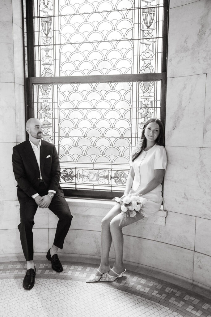 Bride and groom sit by a stained glass window in Minneapolis City Hall