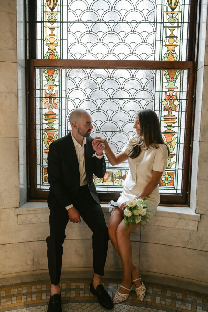 Bride and groom sit by a stained glass window in Minneapolis City Hall