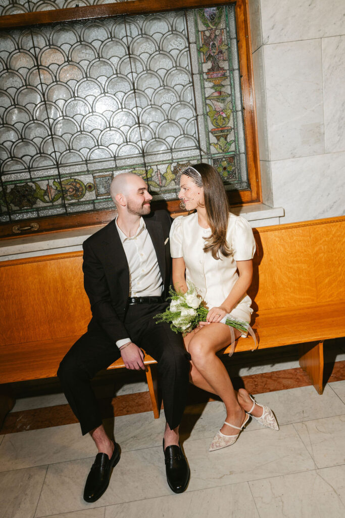 Bride and groom sit on a bench in Minneapolis City Hall waiting for a judge